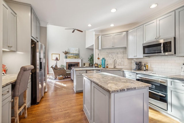 kitchen with appliances with stainless steel finishes, light stone counters, sink, a center island, and light hardwood / wood-style floors