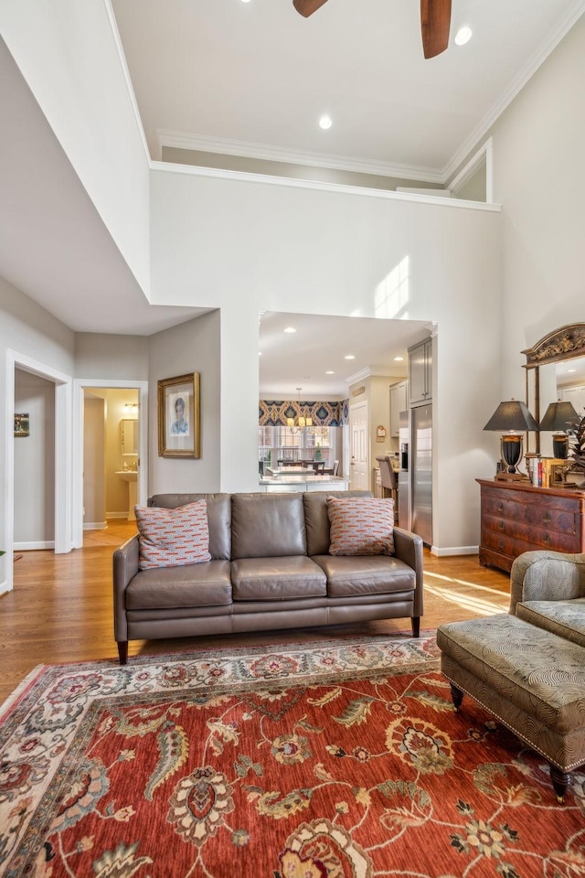 living room with ceiling fan, wood-type flooring, crown molding, and a towering ceiling