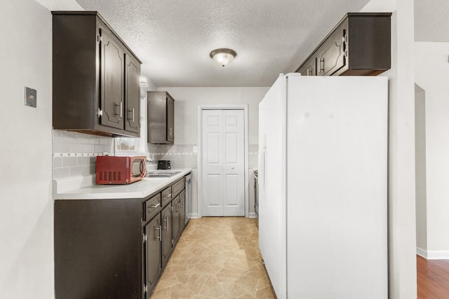 kitchen featuring white refrigerator, tasteful backsplash, dark brown cabinetry, and sink