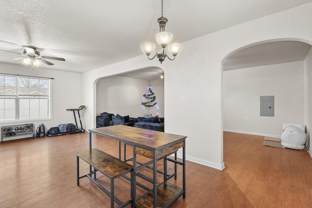 dining area with wood-type flooring, ceiling fan with notable chandelier, electric panel, and a textured ceiling