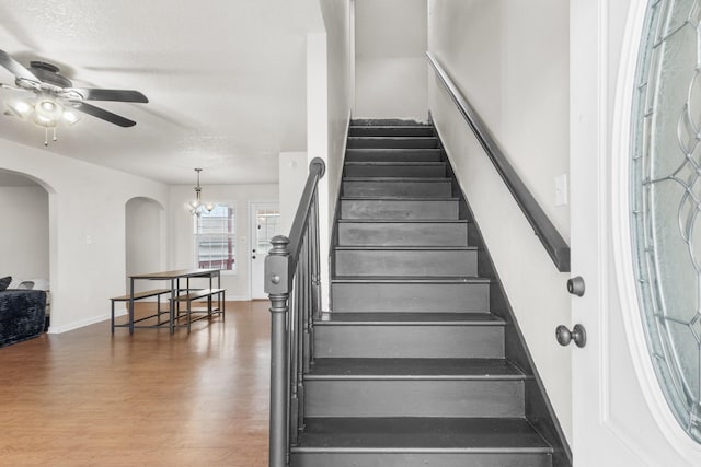 stairway featuring a textured ceiling, ceiling fan with notable chandelier, and wood-type flooring