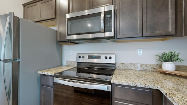 kitchen with dark brown cabinetry, light stone countertops, and stainless steel appliances