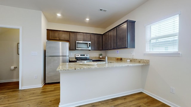 kitchen with hardwood / wood-style floors, dark brown cabinetry, kitchen peninsula, and appliances with stainless steel finishes