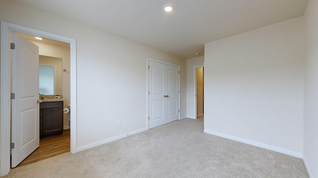 unfurnished bedroom featuring ensuite bathroom, a closet, and light colored carpet