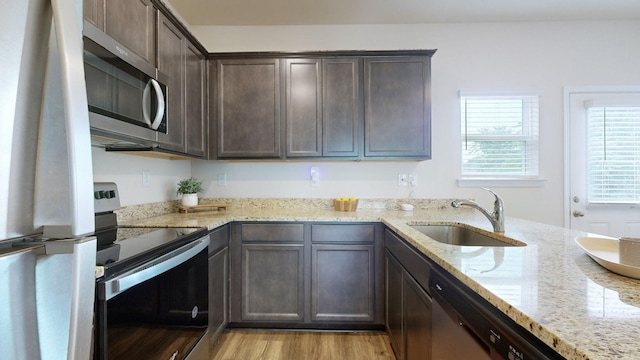 kitchen featuring dark brown cabinets, stainless steel appliances, light stone counters, and sink