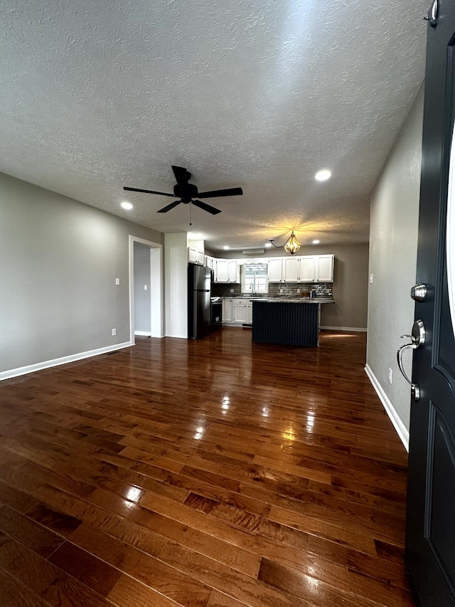 unfurnished living room with ceiling fan, dark hardwood / wood-style flooring, and a textured ceiling