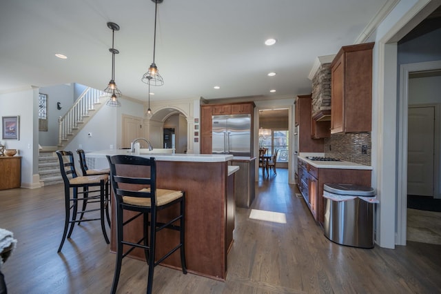 kitchen with backsplash, crown molding, decorative light fixtures, a center island with sink, and built in refrigerator