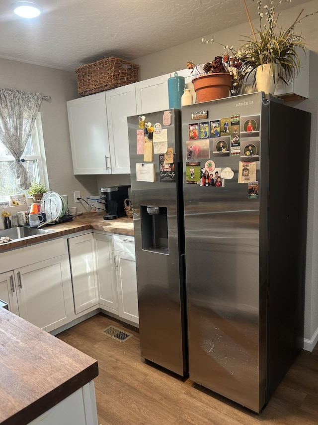 kitchen with white cabinets, stainless steel fridge, light hardwood / wood-style flooring, and sink