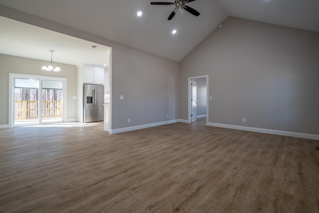 unfurnished living room featuring ceiling fan with notable chandelier, high vaulted ceiling, baseboards, and wood finished floors