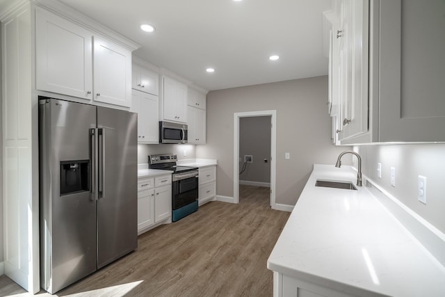 kitchen with recessed lighting, a sink, white cabinets, appliances with stainless steel finishes, and light wood-type flooring