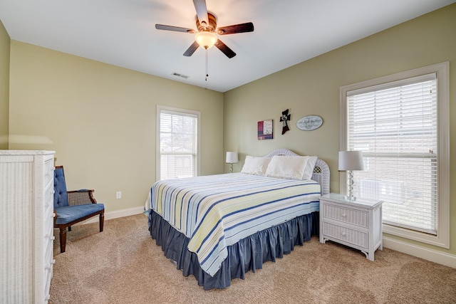 bedroom with ceiling fan, light colored carpet, and multiple windows