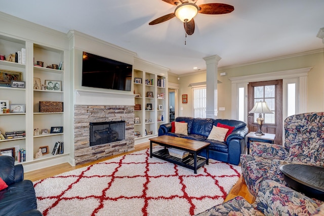 living room with light wood-type flooring, ornamental molding, built in shelves, ceiling fan, and a stone fireplace