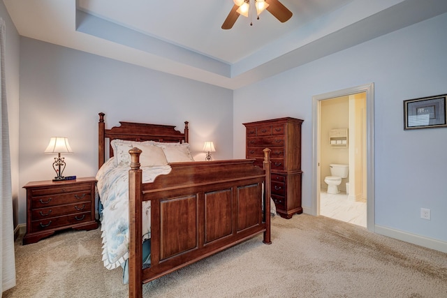 carpeted bedroom featuring a raised ceiling, connected bathroom, and ceiling fan