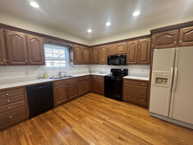 kitchen with tasteful backsplash, ornamental molding, sink, black appliances, and light hardwood / wood-style floors