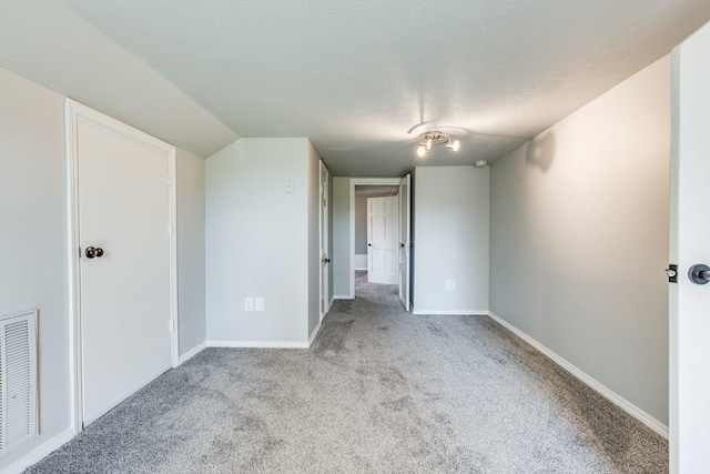 spare room featuring light colored carpet, vaulted ceiling, and a textured ceiling