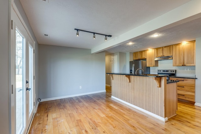 kitchen with a breakfast bar, a textured ceiling, an island with sink, stainless steel appliances, and light hardwood / wood-style floors