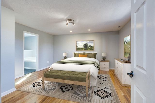 bedroom with ensuite bathroom, a textured ceiling, and light hardwood / wood-style floors