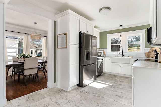 kitchen featuring stainless steel refrigerator with ice dispenser, sink, white cabinets, and decorative light fixtures