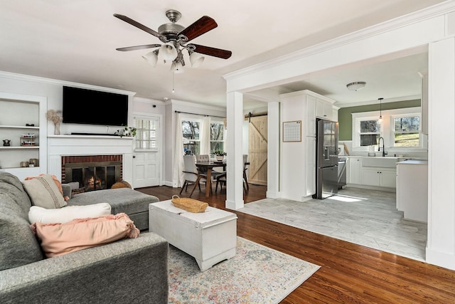 living room featuring crown molding, built in features, ceiling fan, wood-type flooring, and a barn door