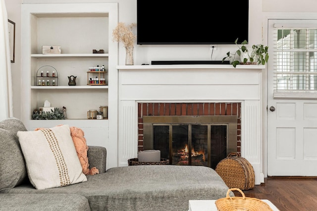 living room featuring dark wood-type flooring, a fireplace, and built in shelves