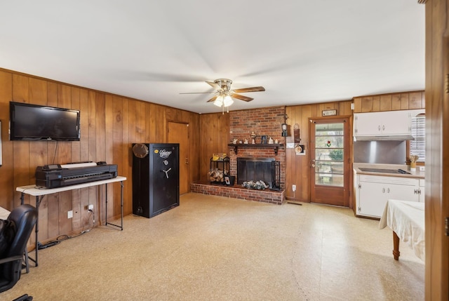 living room with ceiling fan, wood walls, and a brick fireplace