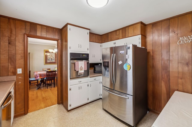 kitchen featuring white cabinetry, stainless steel appliances, and wood walls