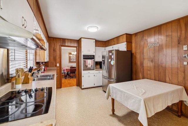 kitchen with stainless steel appliances, white cabinetry, wood walls, and sink