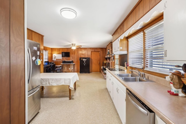 kitchen with wood walls, white cabinets, sink, ceiling fan, and stainless steel appliances