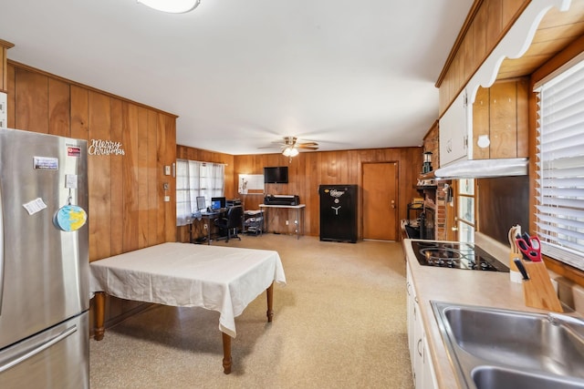 kitchen featuring ceiling fan, sink, stainless steel fridge, wood walls, and black electric stovetop