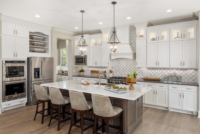 kitchen with appliances with stainless steel finishes, decorative light fixtures, white cabinetry, and an island with sink