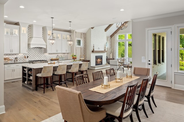 dining area with lofted ceiling, ornamental molding, a fireplace, and light hardwood / wood-style flooring