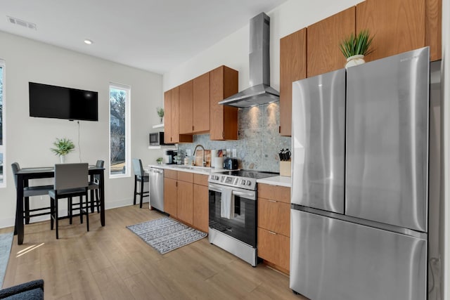 kitchen featuring appliances with stainless steel finishes, backsplash, wall chimney exhaust hood, sink, and light hardwood / wood-style flooring