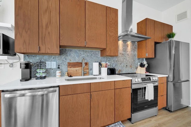 kitchen featuring sink, wall chimney range hood, light hardwood / wood-style flooring, decorative backsplash, and appliances with stainless steel finishes