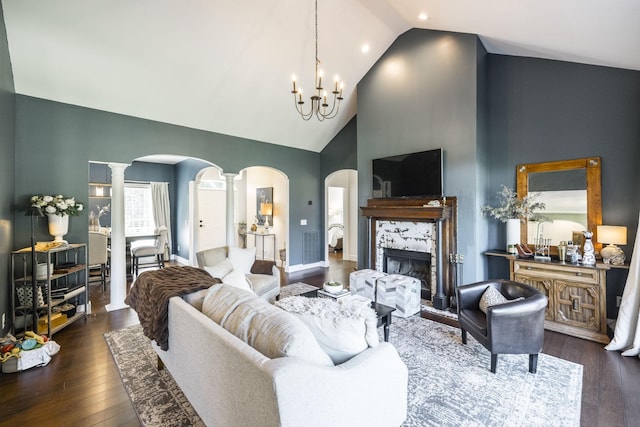 living room featuring dark wood-type flooring, high vaulted ceiling, a tile fireplace, a notable chandelier, and decorative columns