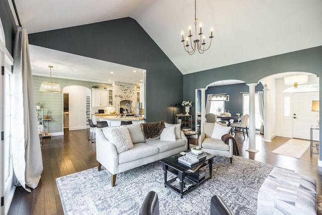 living room featuring ornate columns, high vaulted ceiling, dark hardwood / wood-style floors, and an inviting chandelier