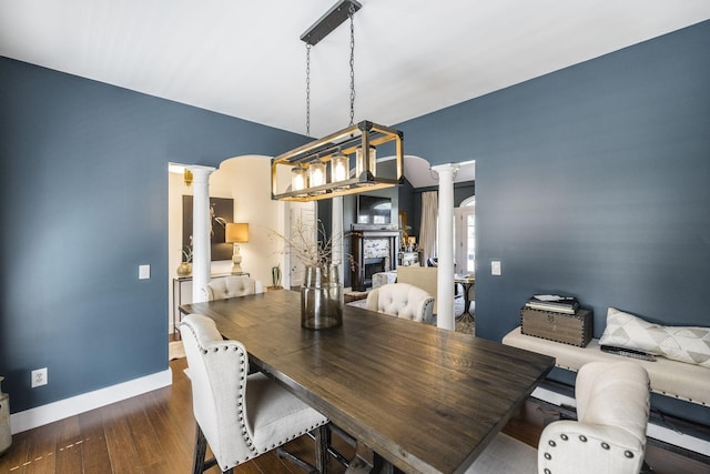 dining area featuring decorative columns and dark wood-type flooring