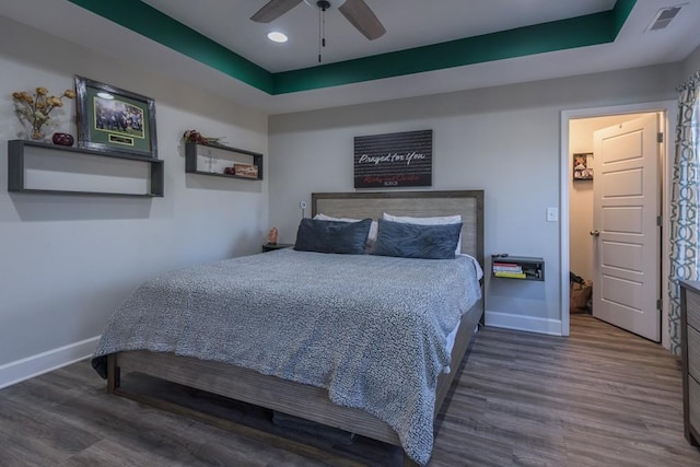 bedroom with ceiling fan, a tray ceiling, and dark wood-type flooring