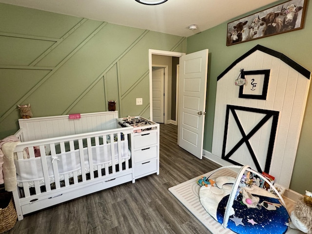 bedroom with a crib and dark wood-type flooring