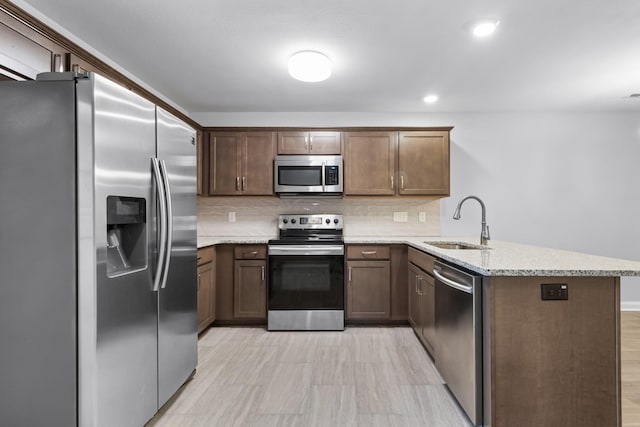 kitchen with light stone countertops, sink, tasteful backsplash, kitchen peninsula, and appliances with stainless steel finishes