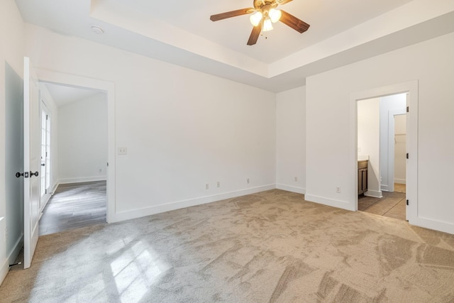 unfurnished bedroom with ceiling fan, a raised ceiling, light colored carpet, and connected bathroom