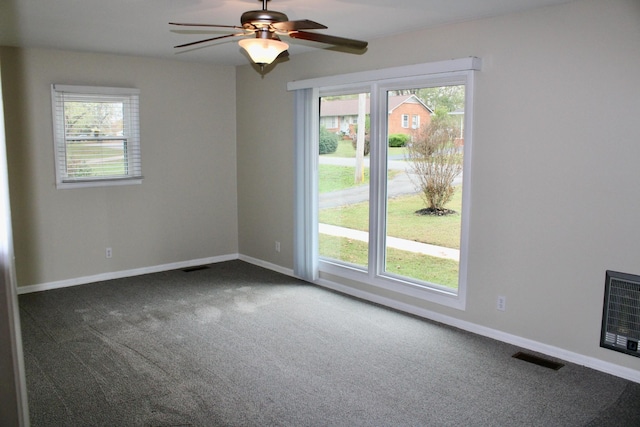 unfurnished room featuring ceiling fan, dark carpet, and heating unit