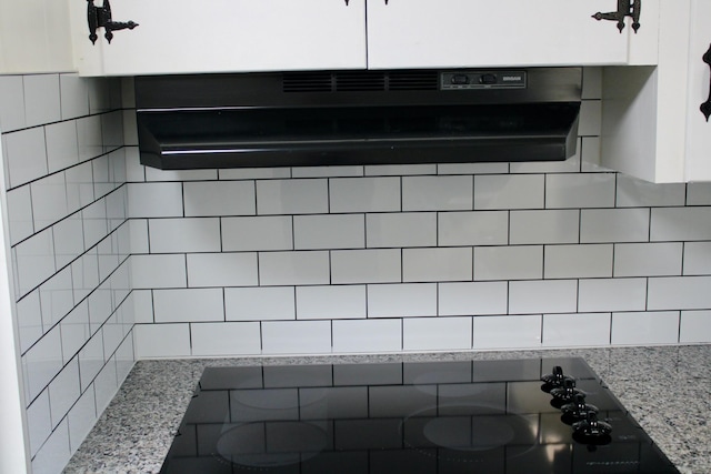 room details featuring backsplash, light stone counters, white cabinets, and extractor fan