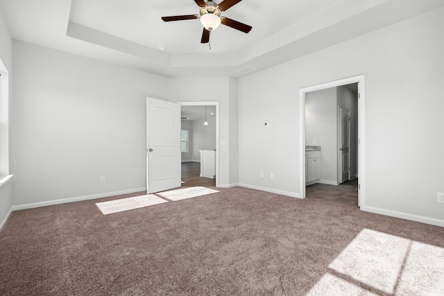 unfurnished bedroom featuring dark colored carpet, ensuite bathroom, a raised ceiling, and ceiling fan