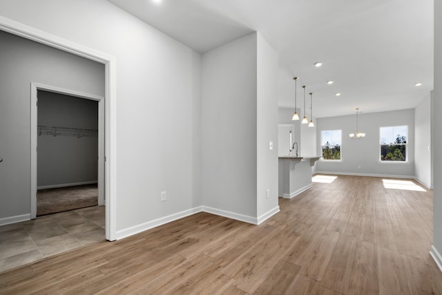 unfurnished living room with a chandelier, sink, and light hardwood / wood-style flooring