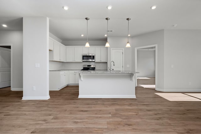 kitchen with white cabinetry, stainless steel appliances, light hardwood / wood-style floors, decorative backsplash, and a center island with sink