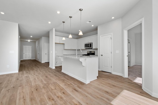 kitchen featuring light stone countertops, stainless steel appliances, an island with sink, light hardwood / wood-style floors, and white cabinets