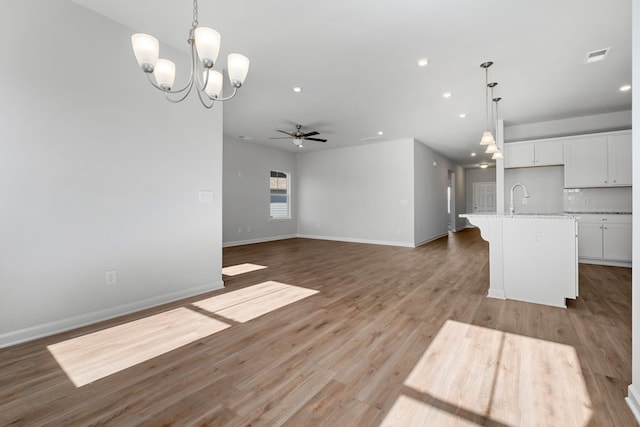 unfurnished living room with light wood-type flooring, ceiling fan with notable chandelier, and sink