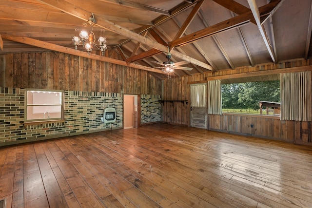 unfurnished living room featuring ceiling fan with notable chandelier, wood-type flooring, vaulted ceiling with beams, and wooden walls