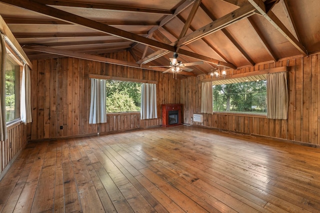 unfurnished living room with vaulted ceiling with beams, wooden walls, a fireplace, ceiling fan with notable chandelier, and hardwood / wood-style flooring