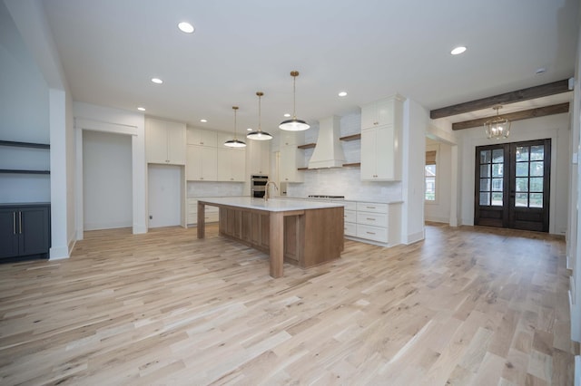 kitchen featuring white cabinetry, french doors, premium range hood, a large island with sink, and decorative light fixtures